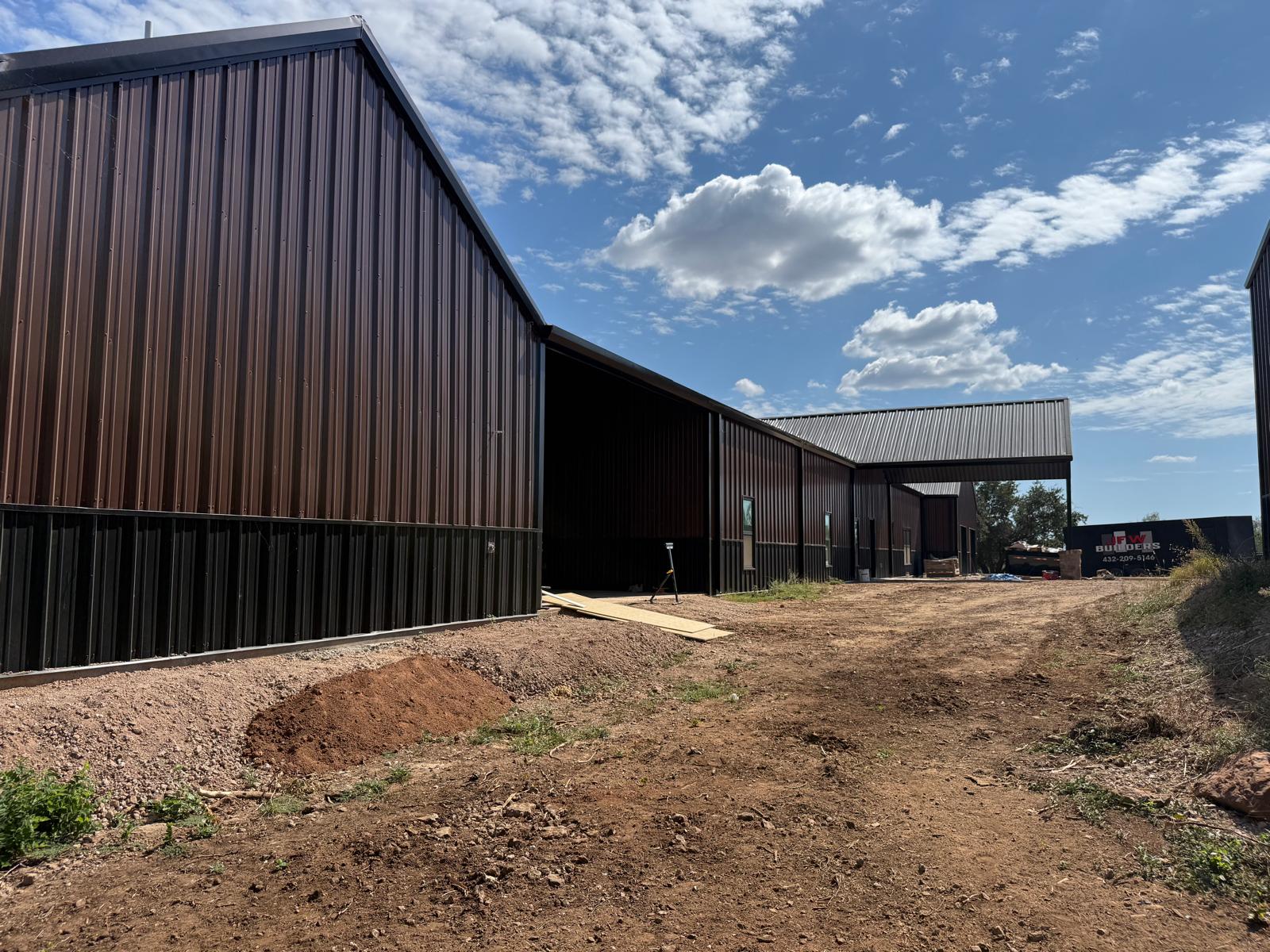 Dark brown metal buildings under construction on a dirt lot outside Seminole, Texas