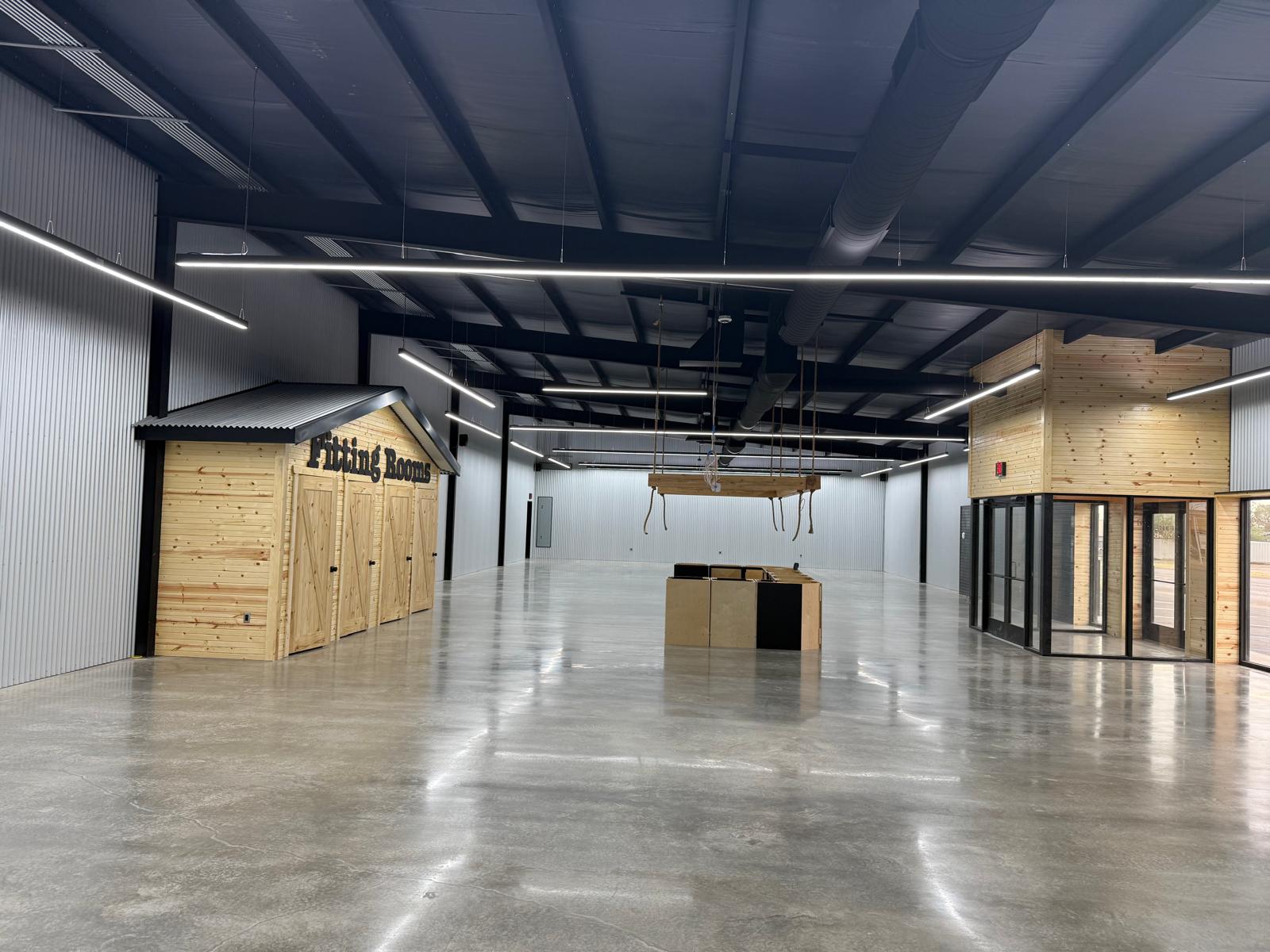 Finished metal building interior with polished concrete floor, white ribbed walls, exposed black steel framing, and linear lighting