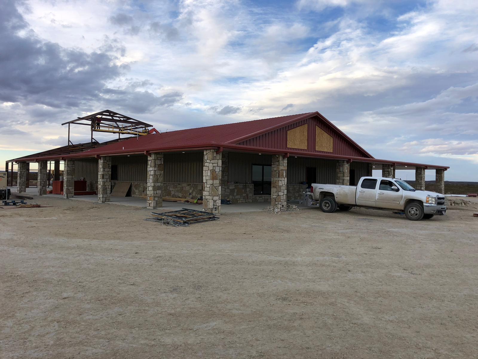 Metal building under construction with a red metal roof, stone columns and a covered porch near Seminole, Texas