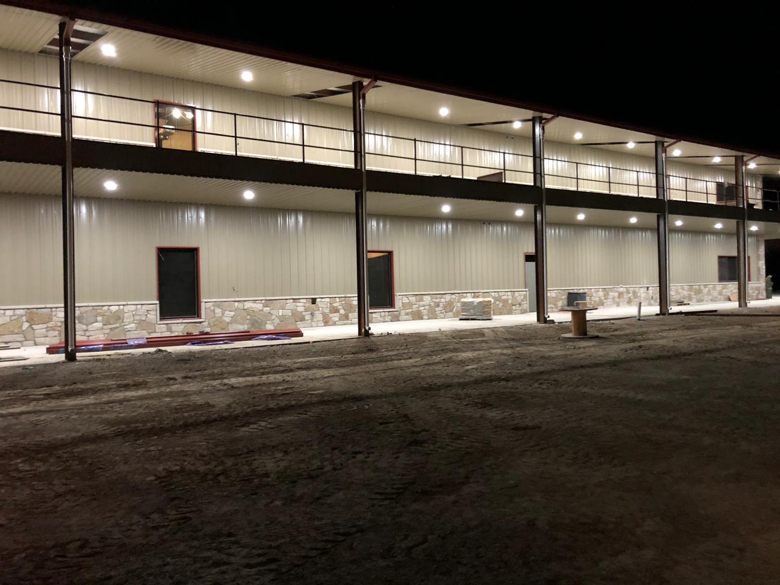 Two-story metal building exterior at night with stone wainscot and balcony railings